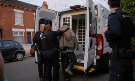 A man being put in the back of a white security van by officers