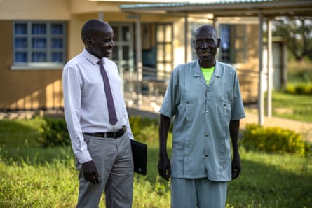Two men smile at each other as they stand outside a yellow building.