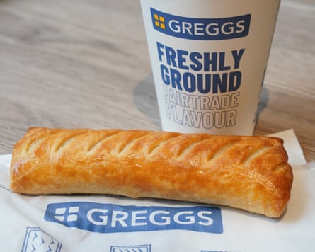 A cup of coffee and a sausage roll on a napkin in a Greggs store