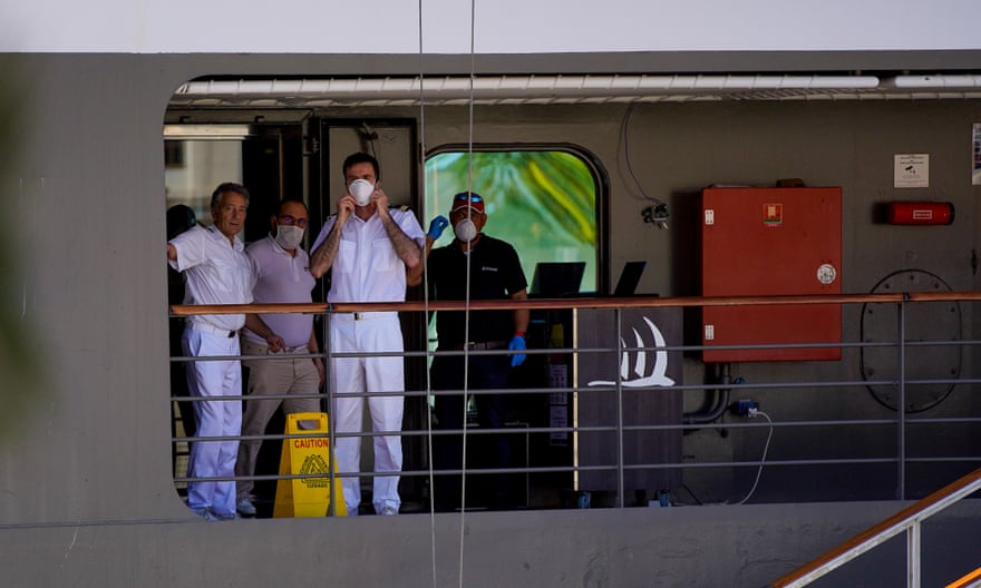 Crew members aboard a luxury cruise ship docked in Rio de Janeiro, Brazil, wear protective masks and gloves.