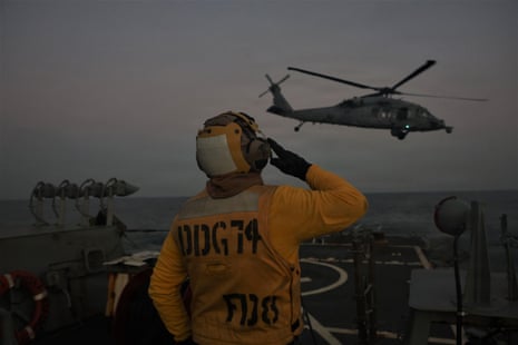 In this handout photograph released by the US Navy on February 3, 2026, a US Navy Gas Turbine Systems technician assigned to Arleigh Burke-class guided-missile destroyer USS McFaul directs an MH-60S Sea Hawk helicopter attached to Helicopter Sea Combat Squadron (HSC) 21.7 during night time flight operations in the Arabian Gulf on January 30, 2026.