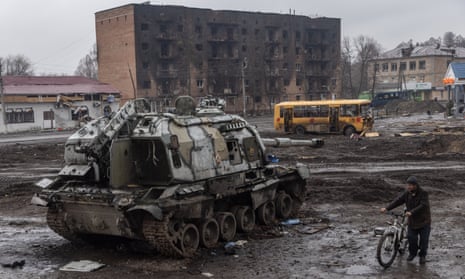 A man pushes his bike through mud and debris past a destroyed Russian self-propelled gun in front of the central train station in Trostianets, Ukraine, in March.