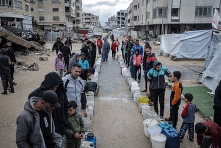 Palestinians wait in the line to fill containers with water distributed by tankers