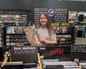 Leoni Horton holds up a vinyl record while standing by the record store section labelled 'Metal'