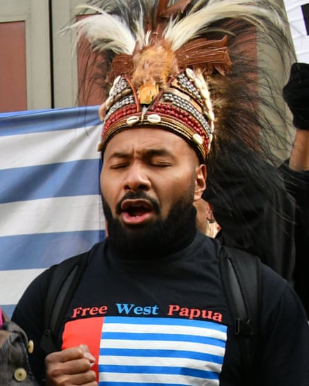 Raki Ap taking part in a protest: he wears a traditional headdress with feathers and beads, plus a black T-shirt with a red, blue and white flag and the words: Free West Papua