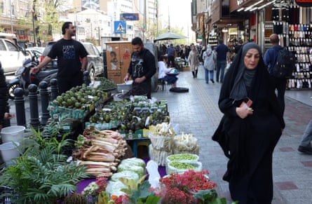 A woman walks past a street stall with fresh fruits and vegetable laid out on it