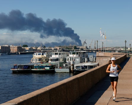 Black smoke billows from a building in the distance as a woman goes for a jog along the river