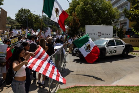 People wave Mexican flags and one person waves a US flag upside as they protest outside a hotel