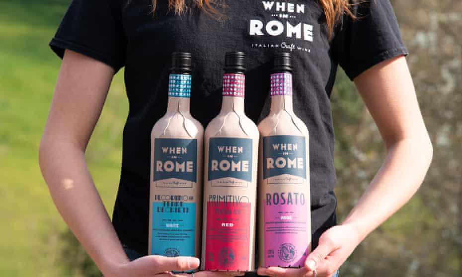 Someone holds When in Rome's paper wine bottles