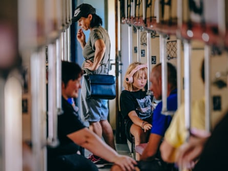 People seated on the train, while a woman stands in the walkway between the seats