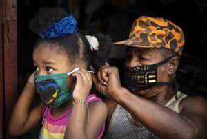 Andres Jimenez, 69, a retired state worker who makes masks to sell in his area, ties a mask on a girl in Havana