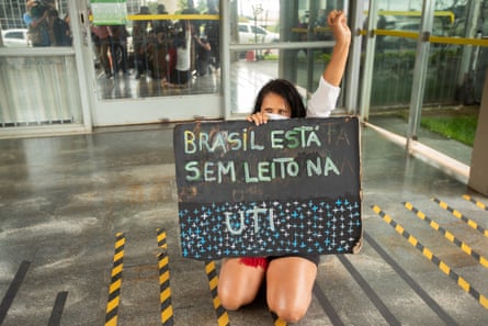 A woman holds a poster that reads “Brazil does not have a bed in the ICU” as she kneels in front of the Ministry of Health in Brasilia, Brazil.