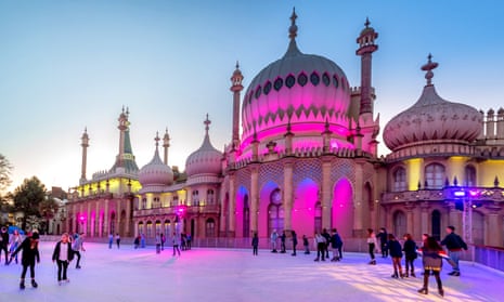 People skating on an ice-rink with the Royal Pavilion in the background, lit up in pink and purple