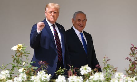 Donald Trump and Benjamin Netanyahu walking together past some flowers. Trump is holding his hand up in a fist, and Netanyahu is smiling