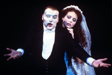 A man in evening dress wearing a white face mask with a woman in a bridal outfit standing behind him