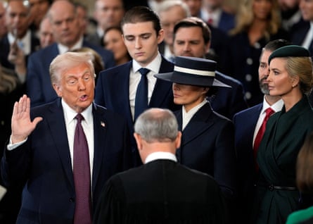 Donald Trump raises one hand as he makes his oath; his son Barron stands behind him and his wife Melania, wearing a dark, wide-brimmed hat, looks on