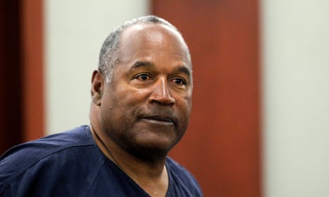 An older Black man in a navy blue prison top, seeming to smile, in a courtroom.