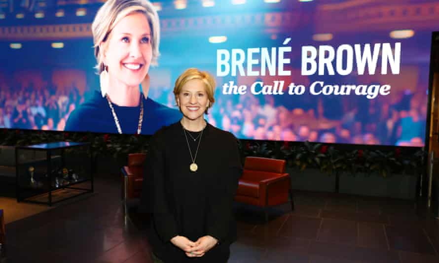 Brown stands in front of image of herself labeled ‘Brené Brown: the Call to Courage’