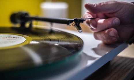 A man's hand about to place the needle of a record player on a vinyl record