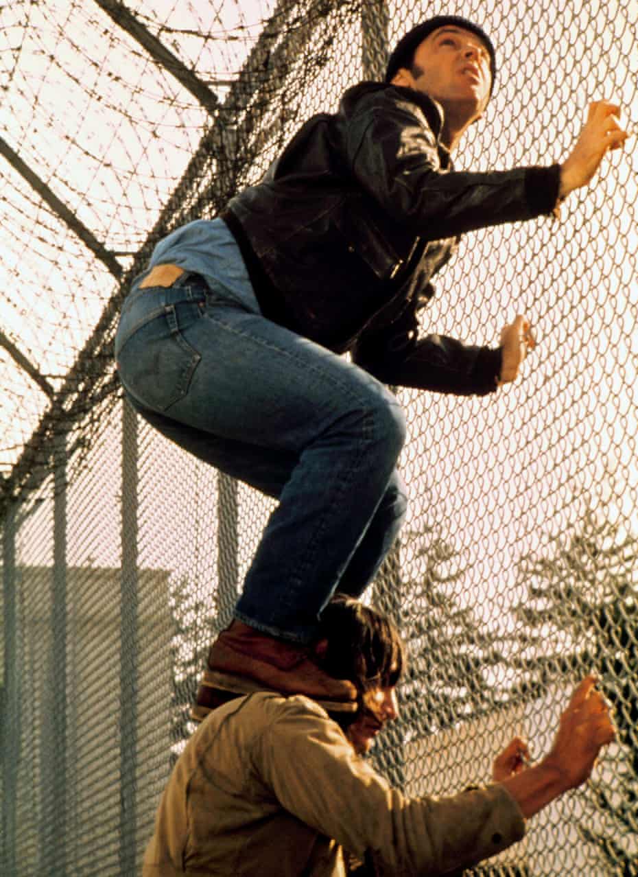 Jack Nicholson standing on the shoulders of Will Sampson, both grabbing a chain-link fence, in One Flew Over the Cuckoo’s Nest