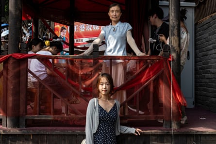 Hao Jingyi stands in front of a wooden balcony, which is draped in red fabric, as her mother stands above her