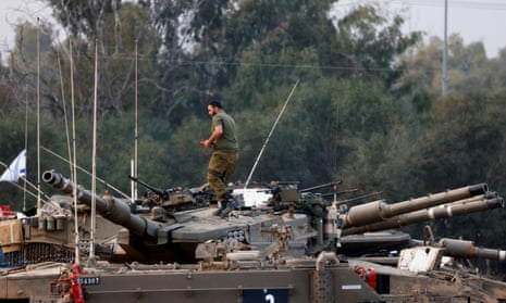An Israeli soldier works atop a tank outside the border with central Gaza