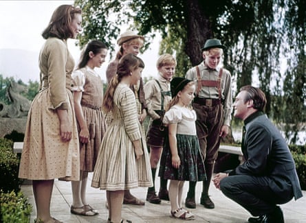 A photo of the Von Trapp family from the film, with Capt von Trapp bending down as he talks to the youngest