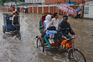 People ride on rickshaw along a street flooded due to heavy rain