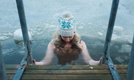 Woman in bobble hat and bikini climbing into the frozen Baltic Sea