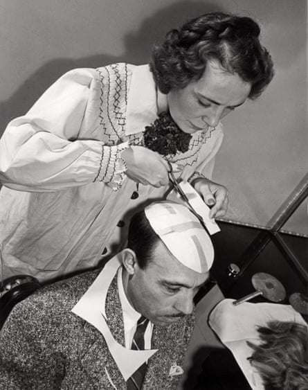 A woman cuts a paper toupee pattern for a man in 1940.