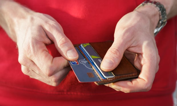 A man in a red top removing a Nationwide bank credit card from a wallet to pay for a purchase