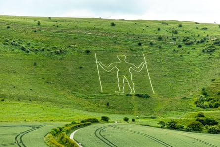 Giant white figure (in chalk) holding poles on green hillside