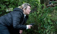 The actor Monica Dolan, armed with a gun, crouches behind a bush in the BBC show Sherwood.