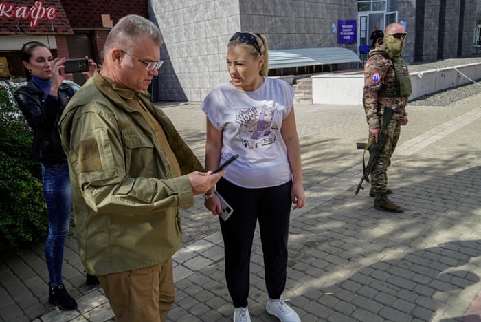 Mayor of Mariupol Konstantin Ivashchenko (L, front) checks a mobile phone as he stands near a woman and an armed serviceman (R) at an outdoor “polling station” in occupied Mariupol.