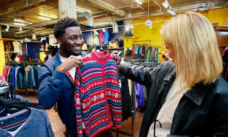 A young man trying on a brightly coloured jumper in a vintage fashion store.
