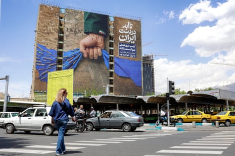 A woman crosses a street in Tehran near a billboard on the facade of a building depicting the strait of Hormuz with a caption in Persian reading “Forever in Iran’s Hand”.