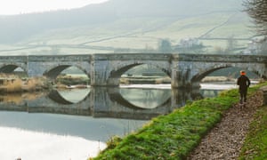 Woman trail running by river, North Yorkshire