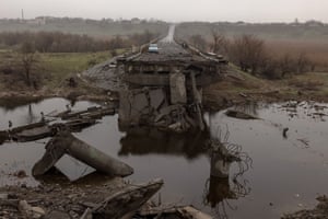 People stand near a car on a destroyed bridge outside Kherson, Ukraine