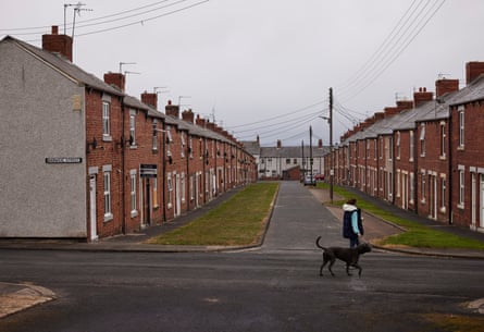 A woman walks a large black dog past terrace houses