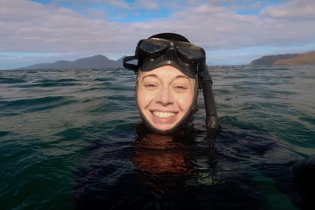 A smiling woman with a snorkelling mask on her head with just her head out of the water.