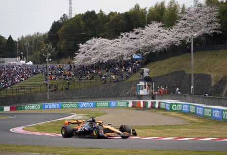 McLaren driver Oscar Piastri in action with a view of cherry blossom in the background.