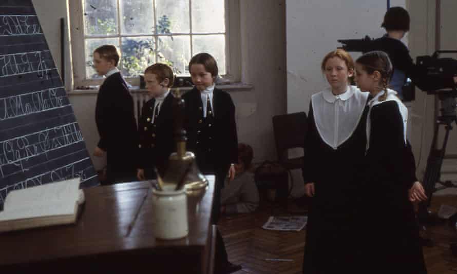 Pupils in old-fashioned uniforms in classroom, camera in background