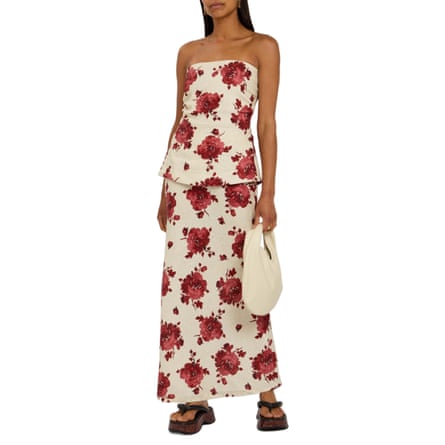 A model wears cream floral-print strapless linen top and floral-printed linen midi skirt. They wear chunky sandals and carry a cream bag.