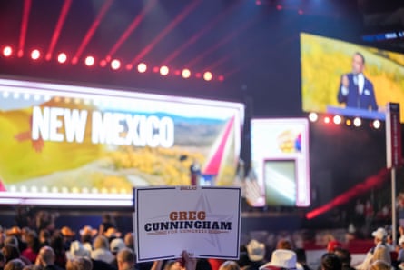 A crowd member holds a Greg Cunningham campaign sign as he speaks on screen nearby