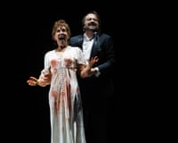 Christine Rice as Judith, wearing a blood-splattered wedding dress and Nathan Berg as Bluebeard, holding her arms in Welsh National Opera’s Bluebeard’s Castle.