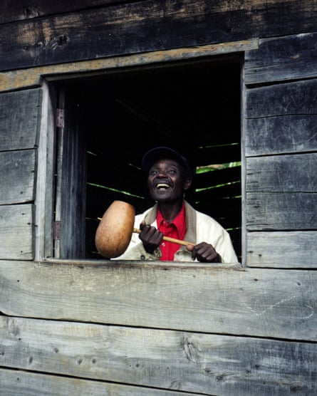 A smiling man holds a stick, at the end of which is a round wooden drinking vessel