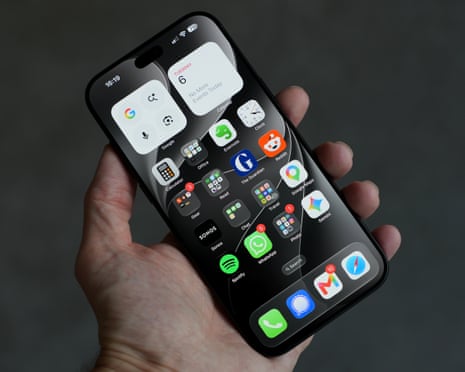 A hand holds a black iPhone 18 Pro Max displaying a home screen full of app icons and widgets.