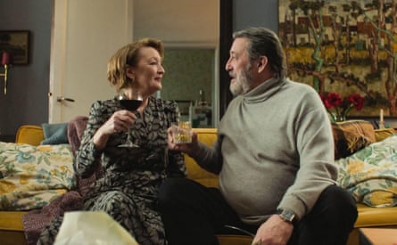 A couple sitting on a bed raise a glass to each other.