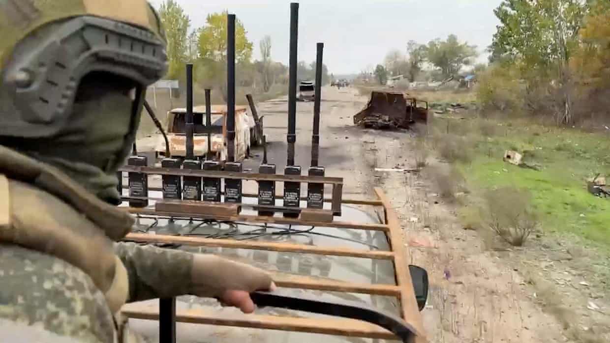 A in a vehicle soldier drives past burnt-out, rusted vehicles abandoned at the side of a road
