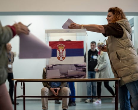A woman casts her ballot into a box decorated with the Serbian flag during elections